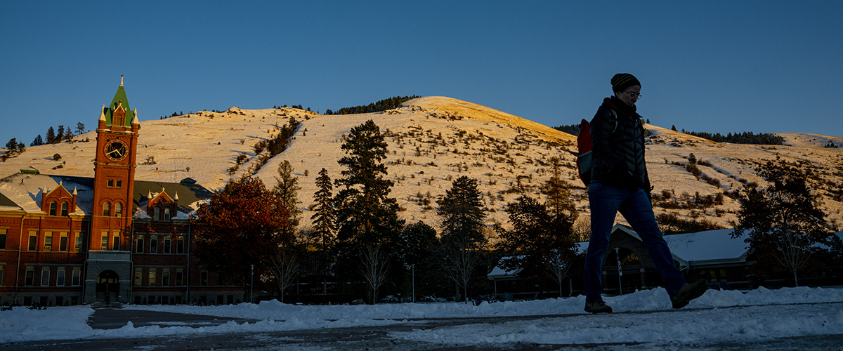 A student walks on the UM campus in the early morning sunlight.