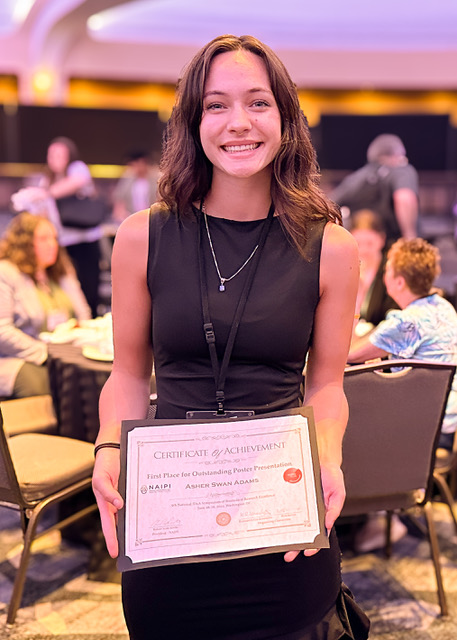 Asher stands in the symposium holding her award.