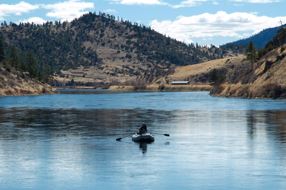 A singular raft floats down the middle of a large river into the sun.