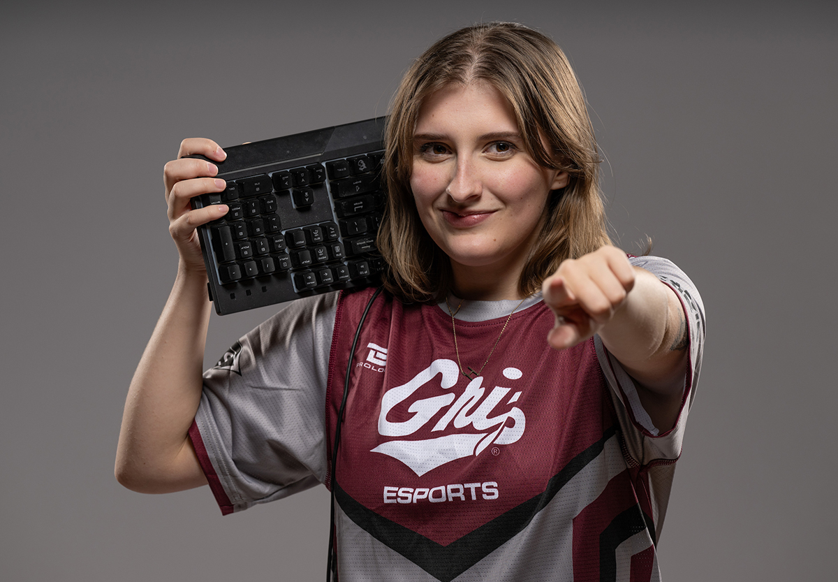 An esports athlete points at the camera while holding a keyboard