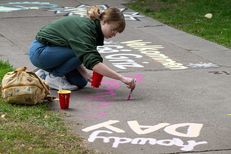 A student paints a greeting on the sidewalk 