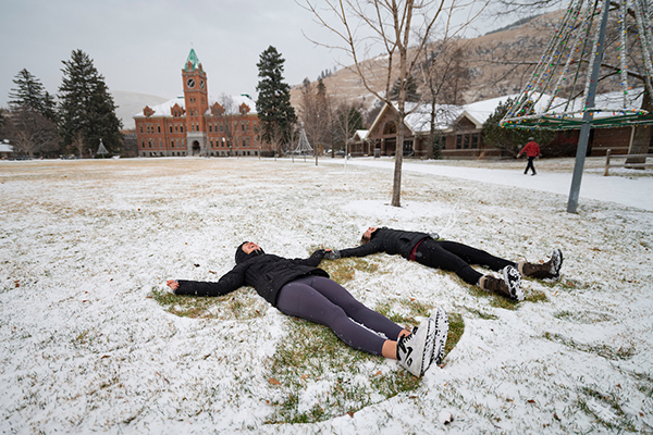 Two students make snow angels in a thin layer of snow on the Oval.