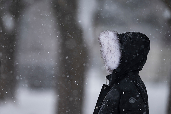 A person stands outside on a snowy day wearing a parka with a fuzzy hood.