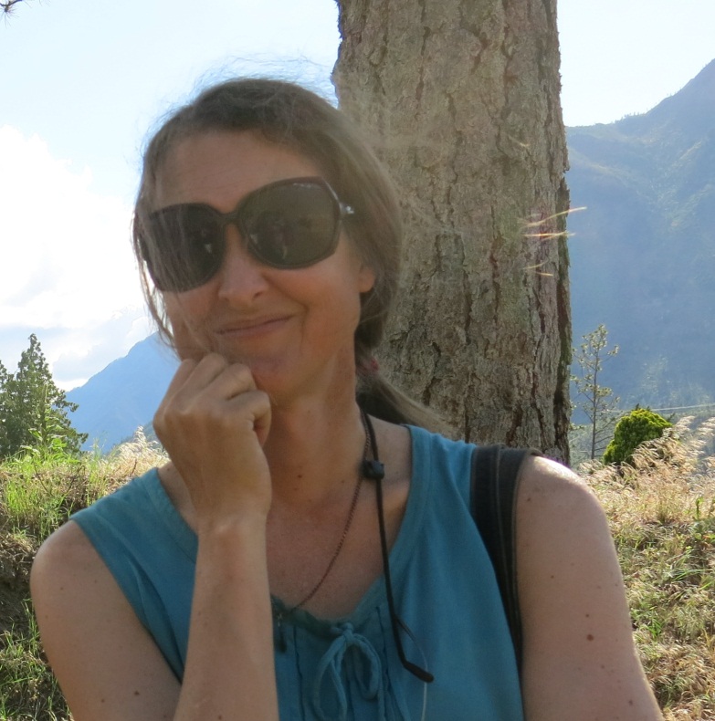 Anna Prentiss wearing sunglasses and a blue top, sitting by a tree with mountains in the background.