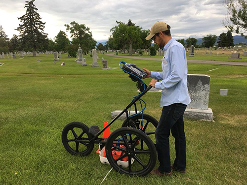 Ethan Ryan operating a ground-penetrating radar cart in a cemetery.