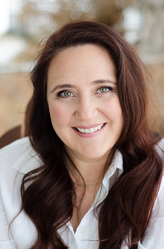 Smiling Dr. Meradeth Snow with long brown hair in a white shirt, outdoors with a softly blurred background.