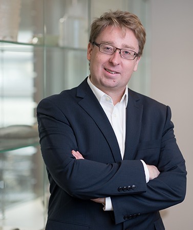 Dr. Michael T. Richards in a dark suit and glasses standing with arms crossed in an office setting.
