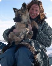 Dr. Natasha Lyons smiling in a winter coat holding a German Shepherd puppy outdoors in the snow.