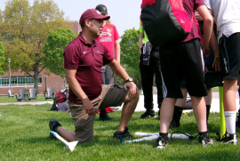 A role model kneels in grass as they demonstrate a rocket-launching activity to a group of middle school students.