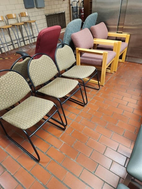 Assorted waiting-room chairs lined up on a brick floor in a storage area.