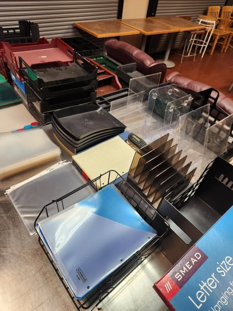 Assorted office supplies on a table, including document trays, file organizers, folders, and a letter-size Mead notebook.