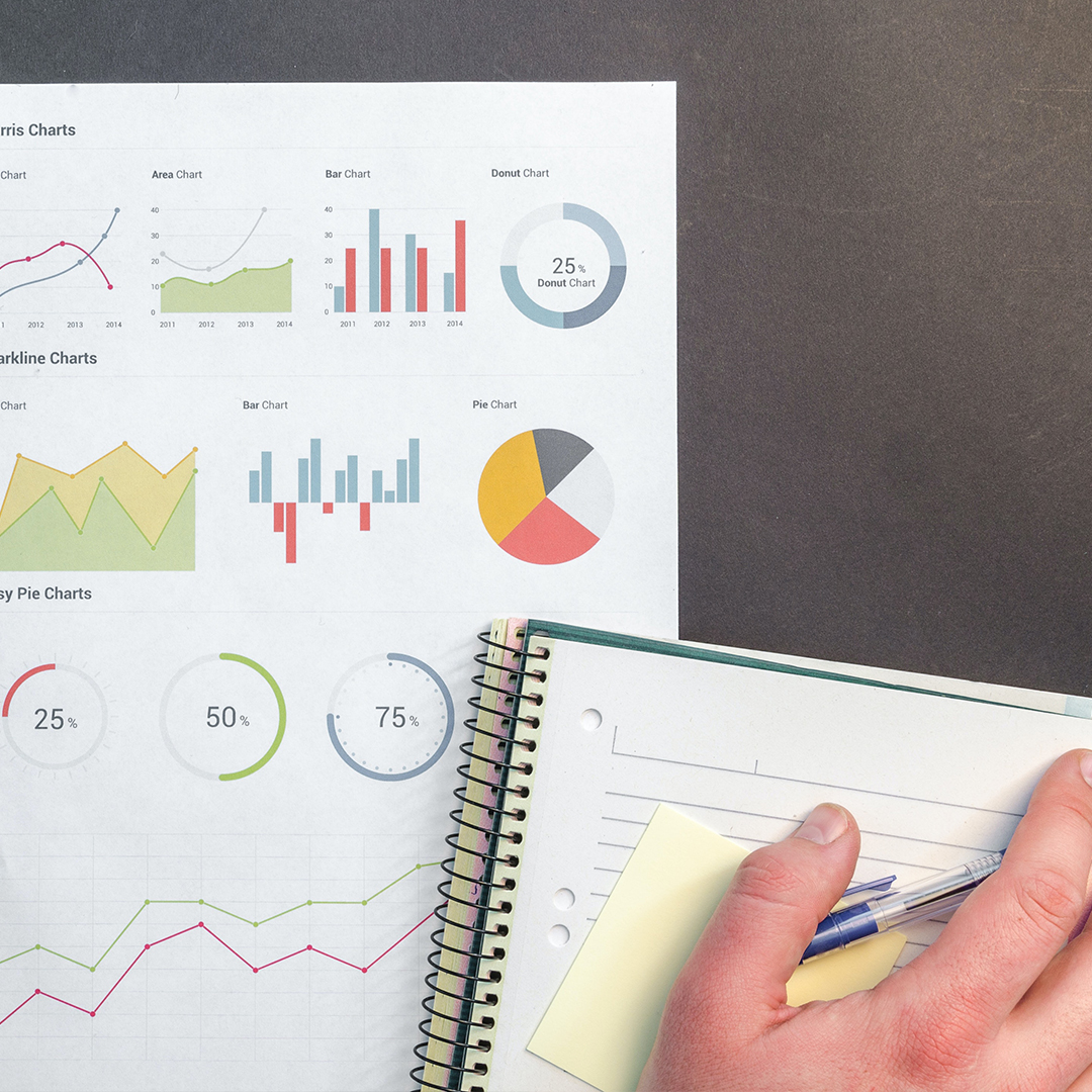 top view of page of graphs and an open notebook with a hand and pen resting on top of it