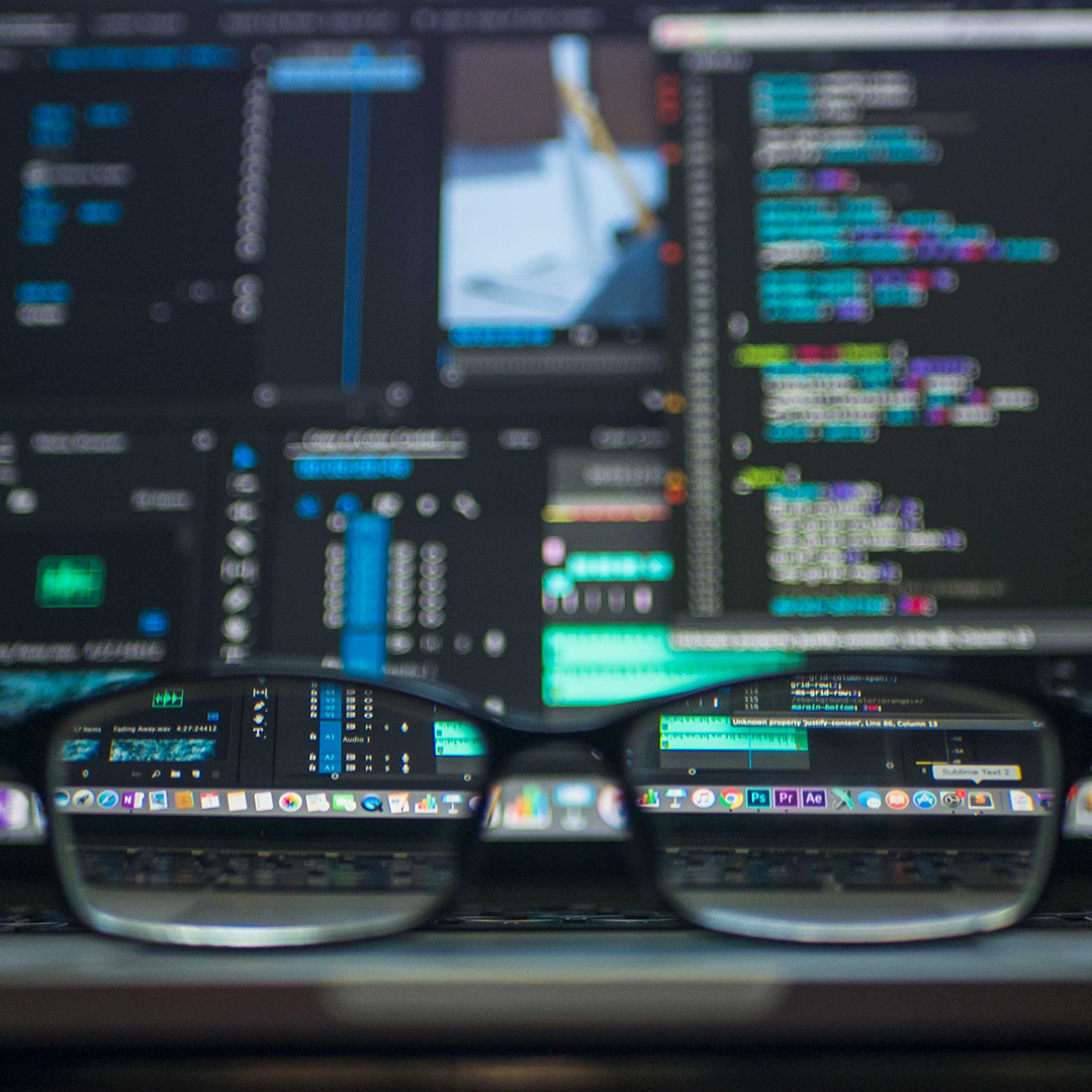 computer screen filled with data and graphs with pair of glasses resting on table in front