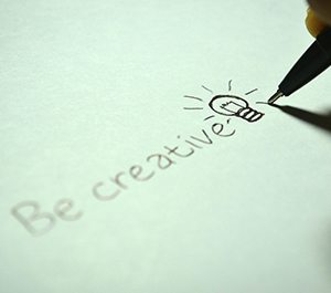 The words "Be Creative" and a picture of a lightbulb are drawn on a piece of paper.