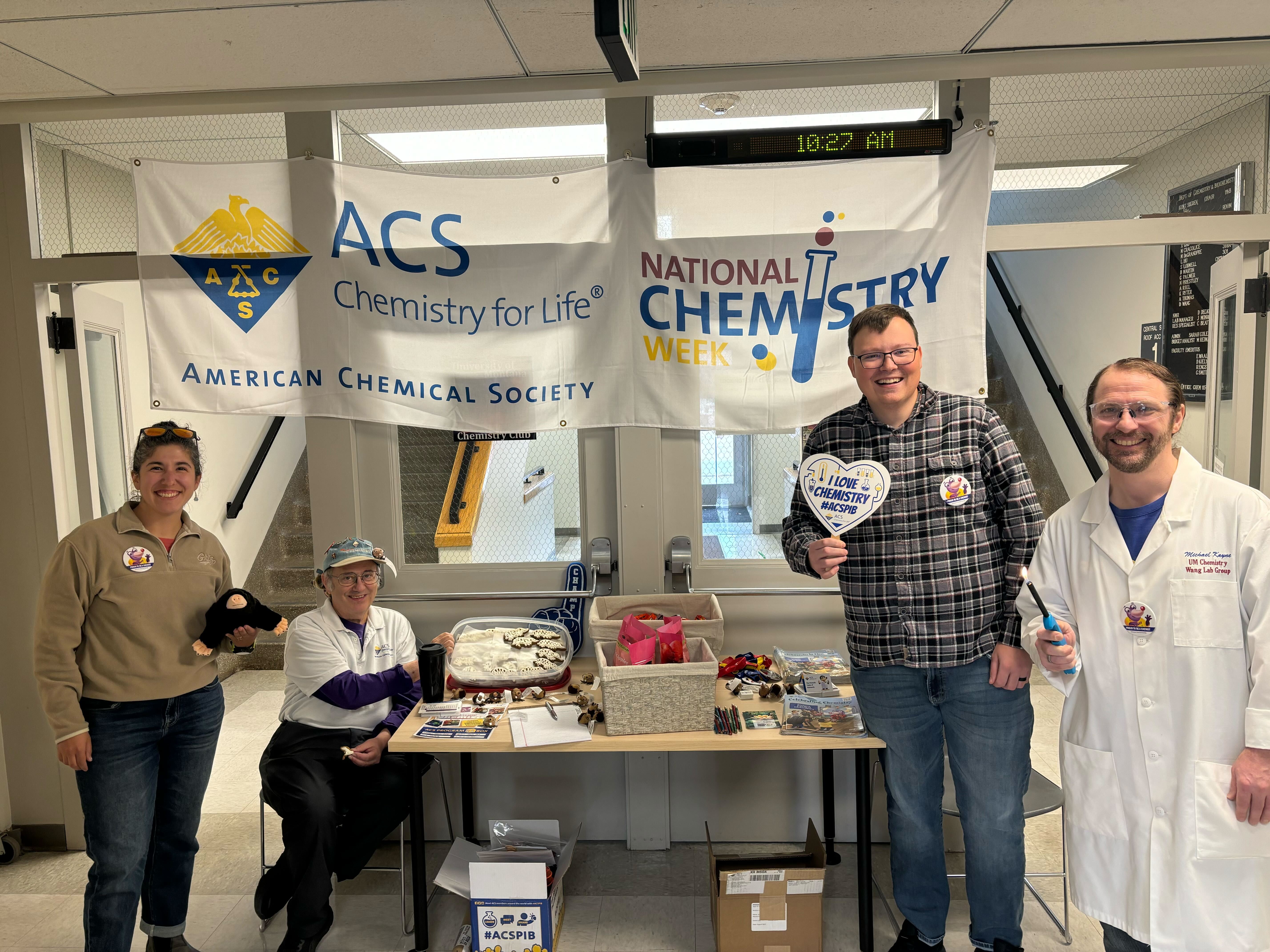 four people smile at camera under chemistry banner