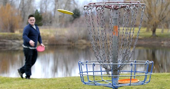 Disc Golfer throwing disc into basket