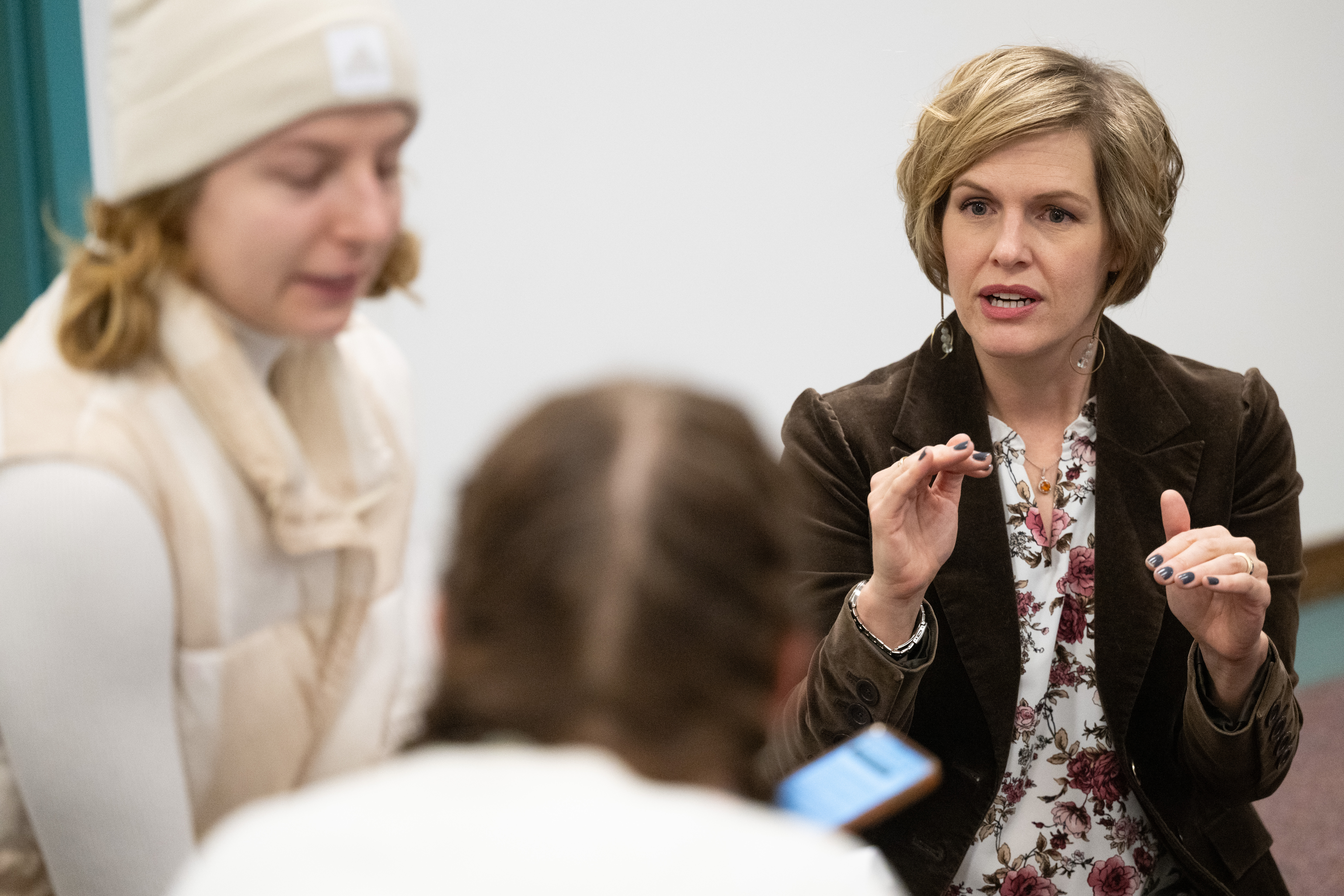Prof. Heather Voorhees kneels to talk with two students in a classroom setting. 