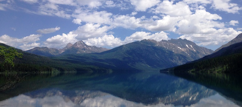 A serene landscape showcasing a tranquil lake surrounded by majestic mountains under a partly cloudy sky.