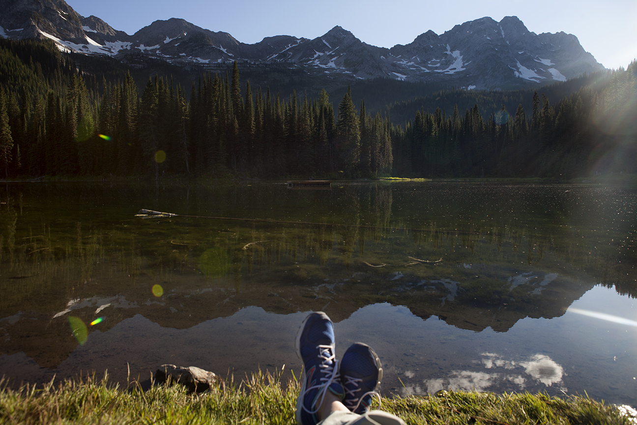 The author's feet in sneakers in front of a lake with mountains in the background