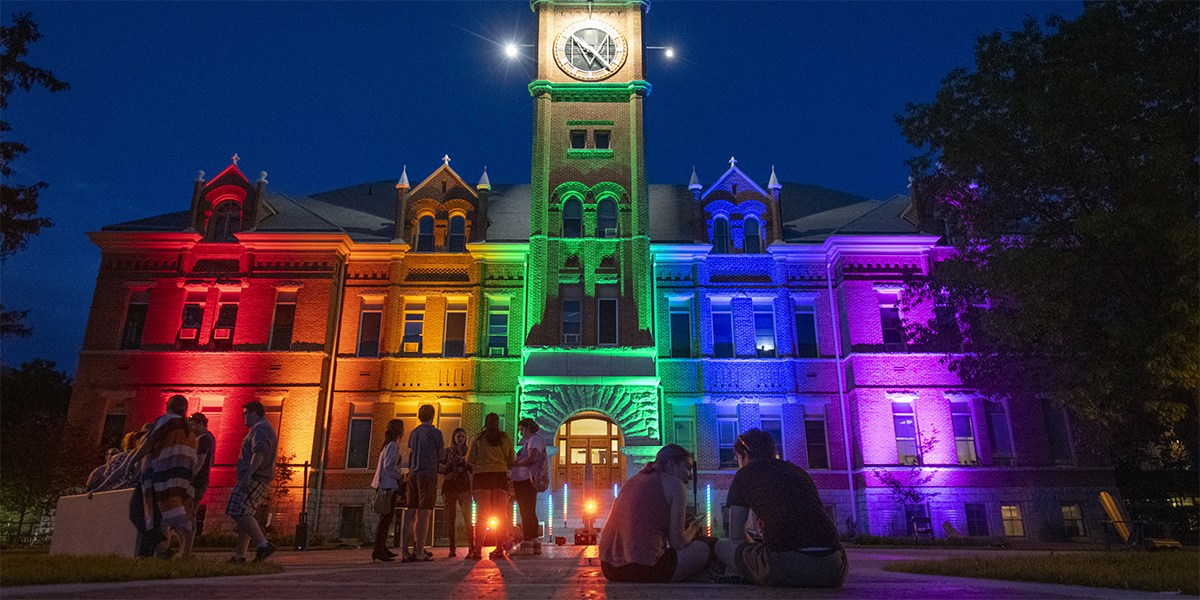 Main Hall lit up for pride week with a rainbow of lights