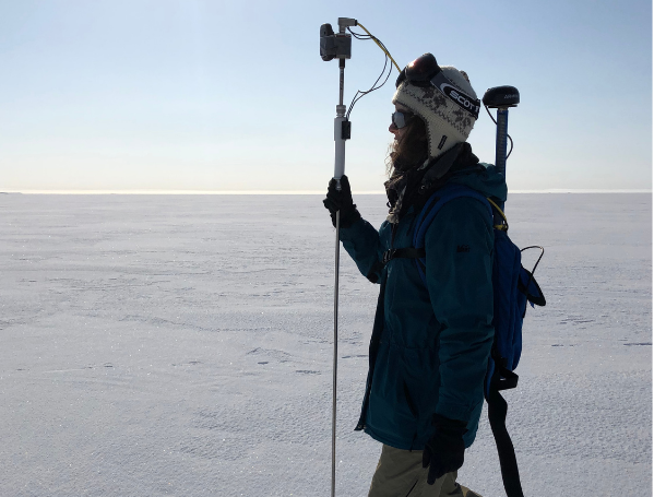 person walking on ice field carrying monitoring equipment