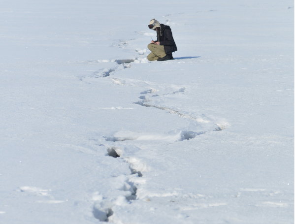 person crouching down and taking notes near a crack in a field of ice