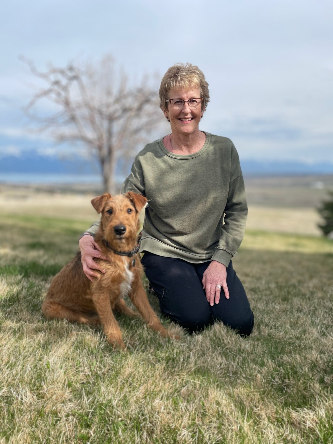 Teresa Morigeau sitting in a field with her arm around her dog.