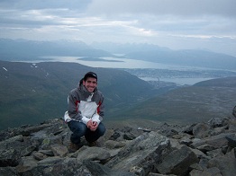A guy squatting for a photo on top of a mountain
