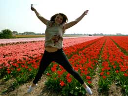 A girl jumping in front a red field of flowers