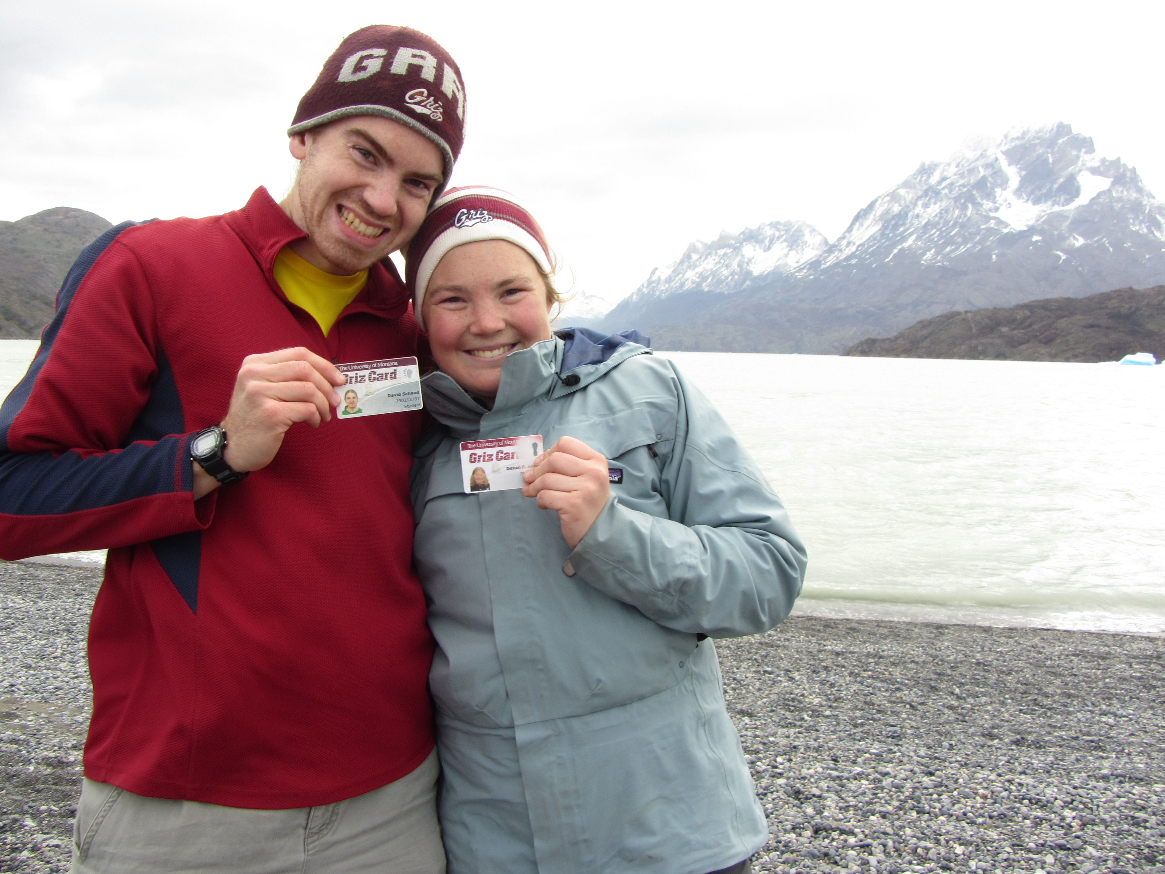 Two UM students pose in front of a mountain with their Griz cards