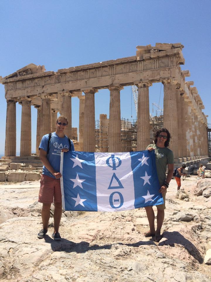 Two students hold fraternity flag in front of panthenon