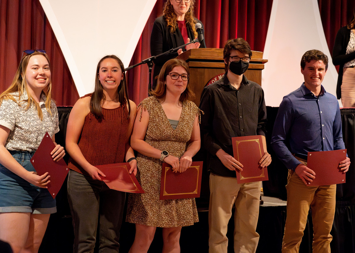 Students stand in front of stage with award certificates
