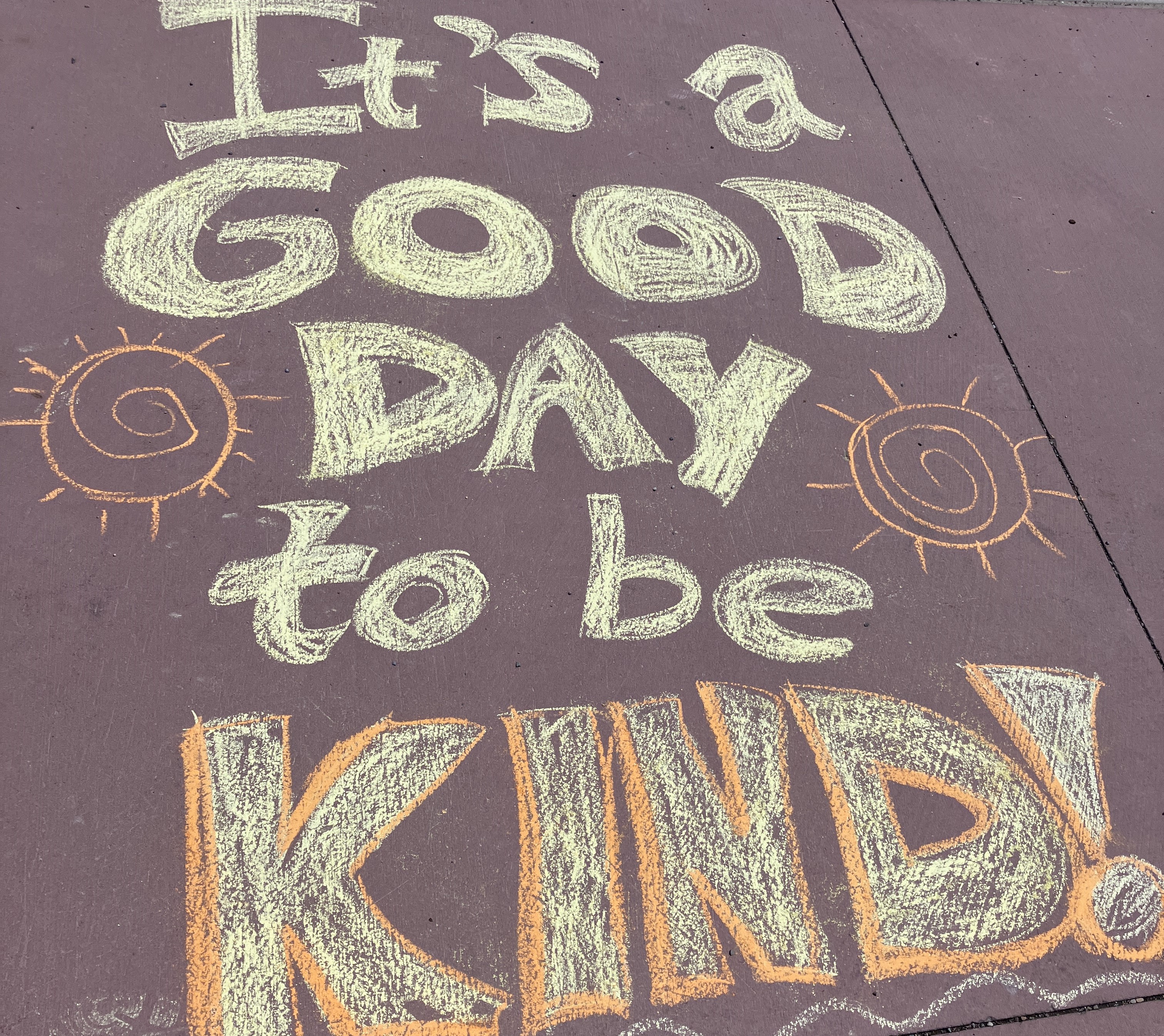 'It's a good day to be kind' written in yellow chalk on the sidewalk