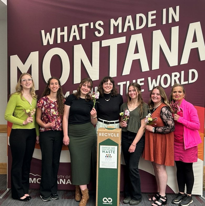 team of six students stands with mentor in front of a UM banner after presenting at the conference for undergraduate research