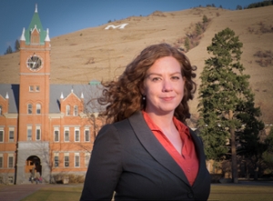 Anisa Goforth in a blazer stands outdoors with University Hall and hillside in the background.