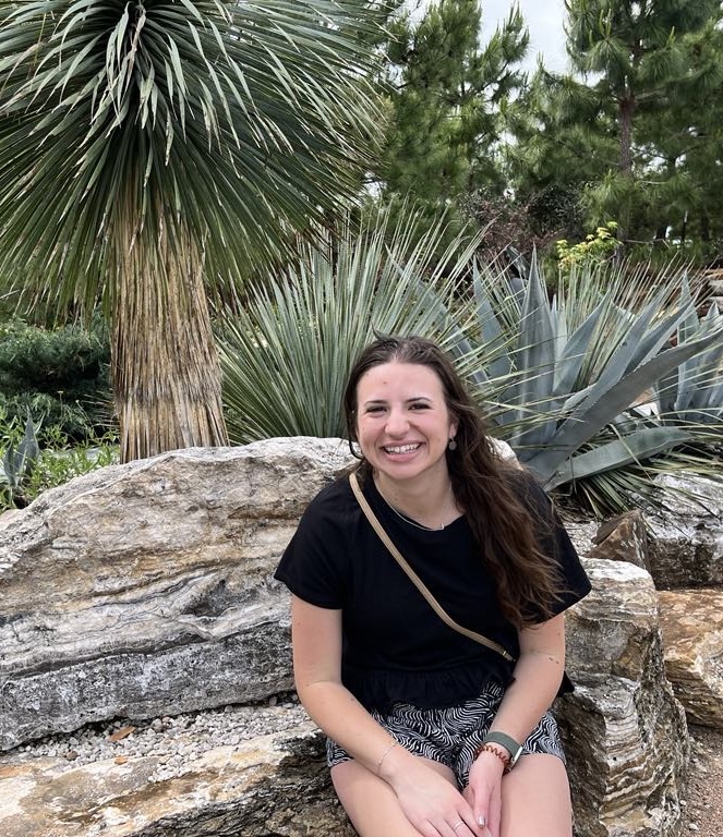 Woman sitting on a rock wearing a black shirt. Behind her are large, sharp plants.