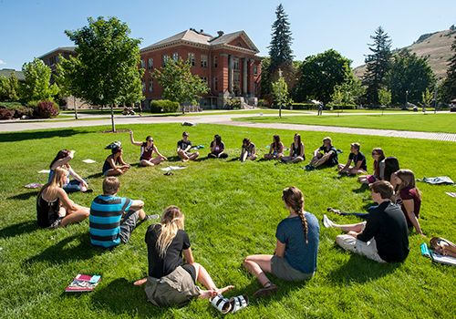 Students sitting in a circle formation on the UM oval