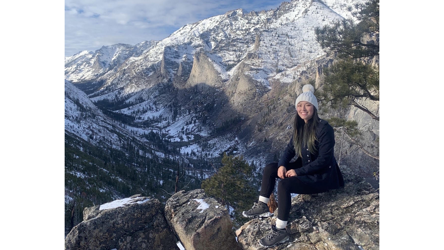 A woman sits on a rock with snow-covered mountains in the background.