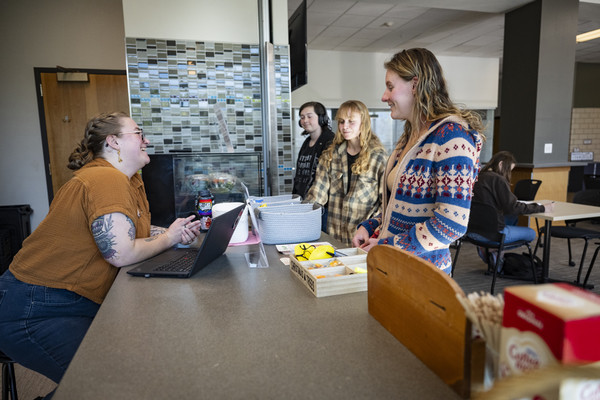 Students interacting with a staff member at a service counter in a modern cafeteria setting.