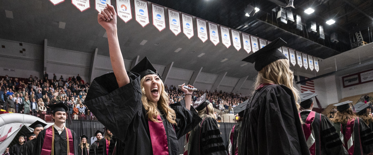 A graduate throws her arms in the air in celebration upon entering the Adams Center for Commencement ceremonies at UM on Saturday, May 14. 