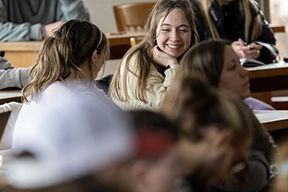 A female student sits in a UM classroom and talks with a classmate. 