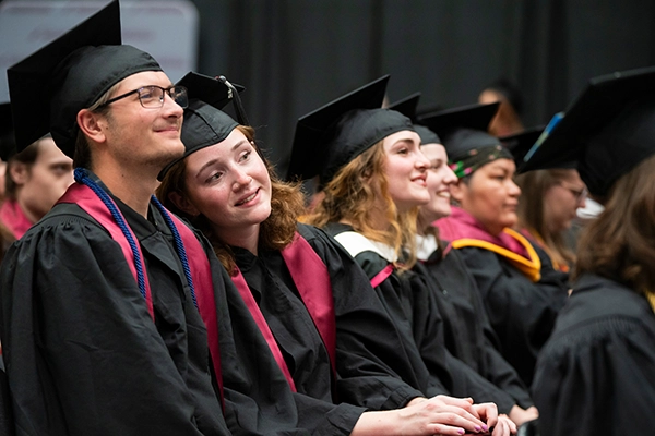 Two students listen to a Commencement speaker during their graduation ceremony
