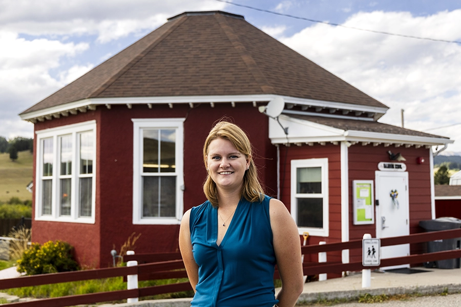 UM grad Alison Bramlet poses before the one-room schoolhouse she teaches at.