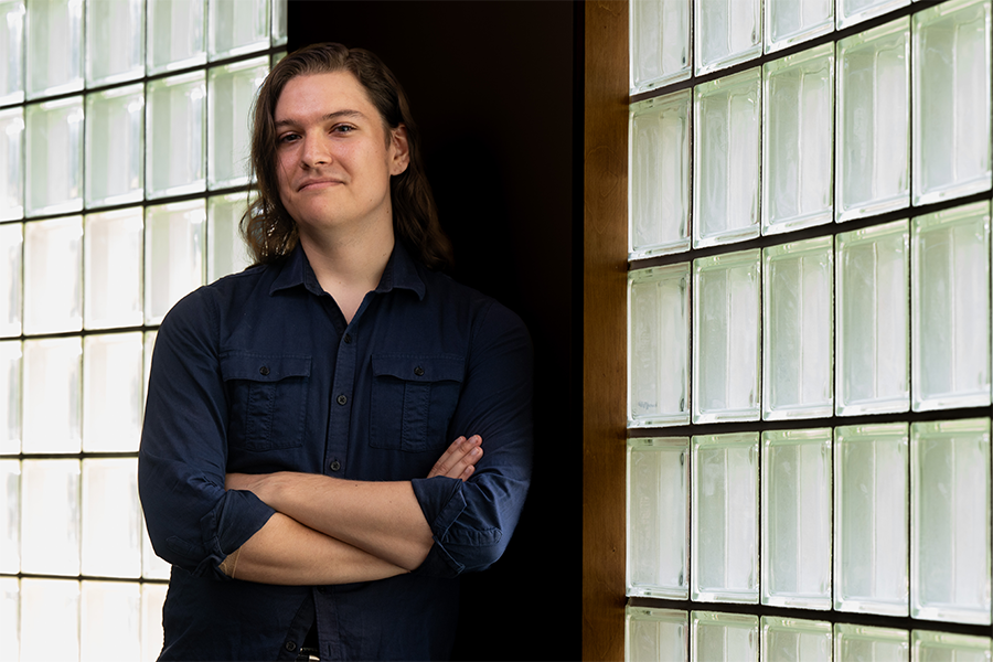 Chris smiling for the camera with their arms crossed, next to brick windows