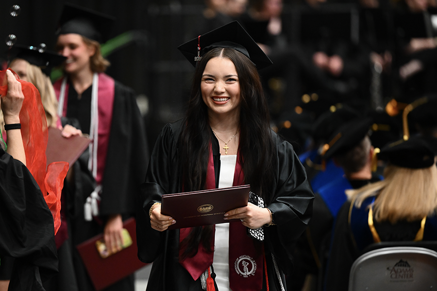 A female graduate walks across the podium on Commencement Day at UM 