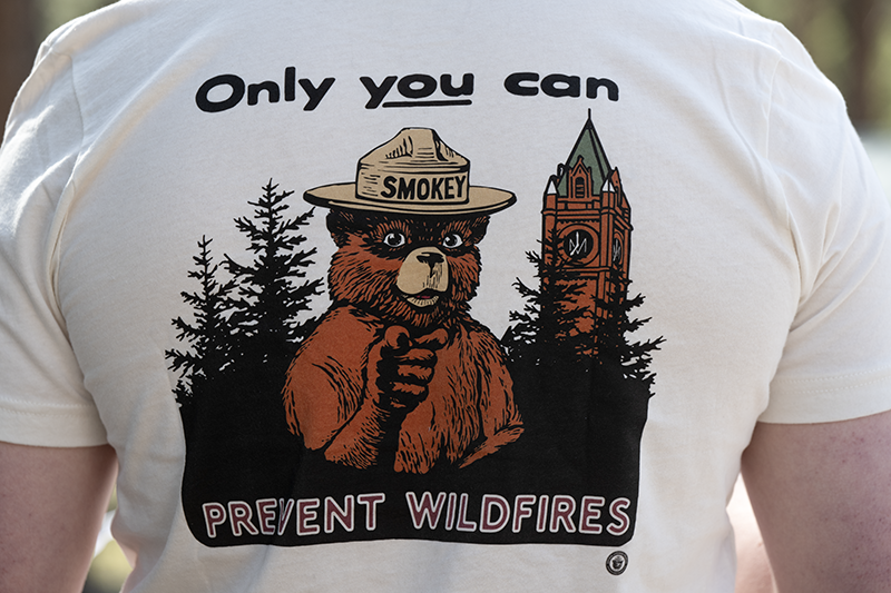 A T-shirt showcasing an illustration of Smokey Bear next to UM's Main Hall