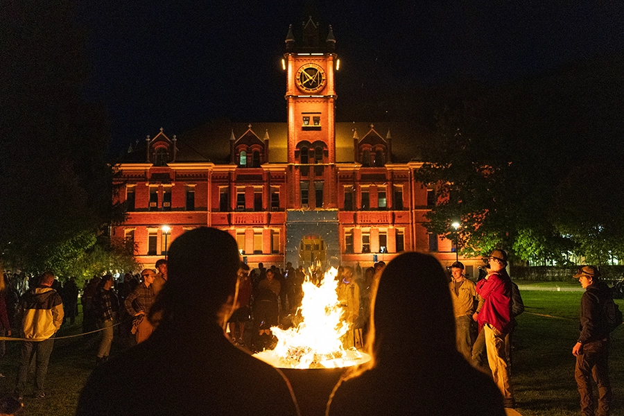 The campus community gathers around a fire in front of Main Hall. 