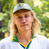 Person smiling in front of green background outside.