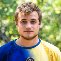 Person smiling in front of green background outside.