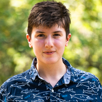 Person smiling in front of green background outside.